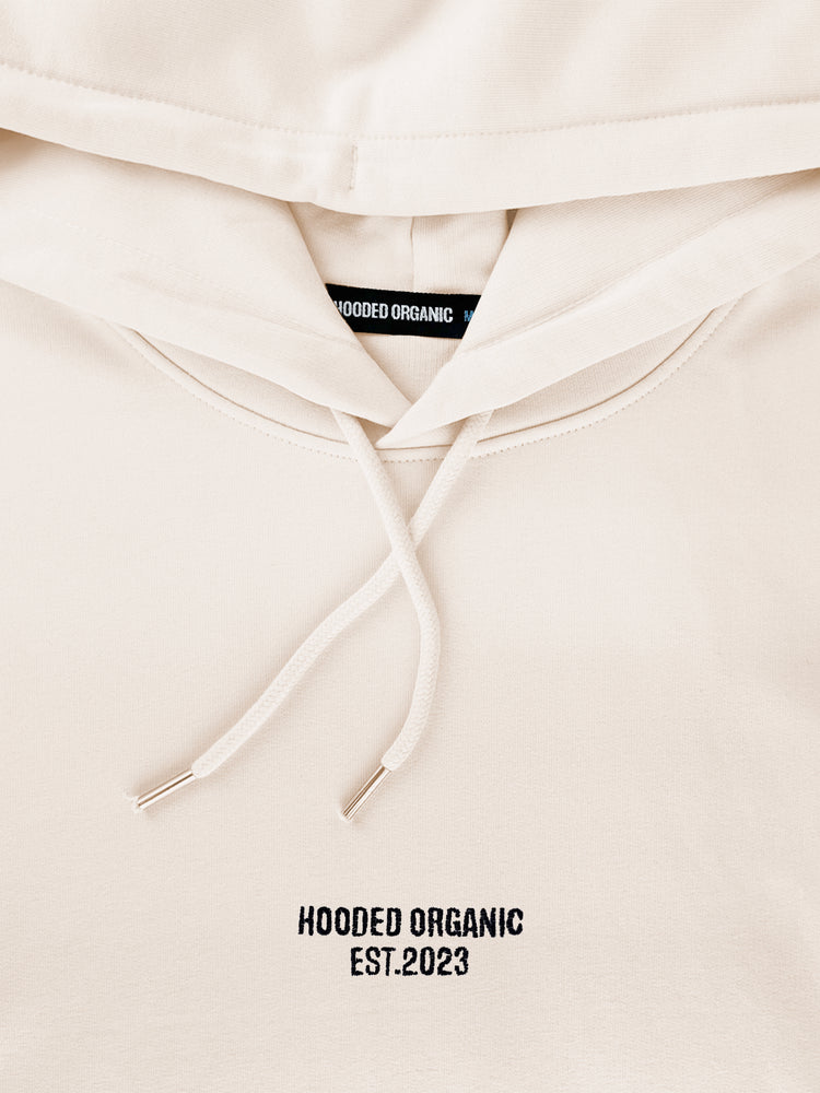 Nærbillede af Hooded Organic-logo på beige hoodie – lavet i 100% økologisk bomuld
