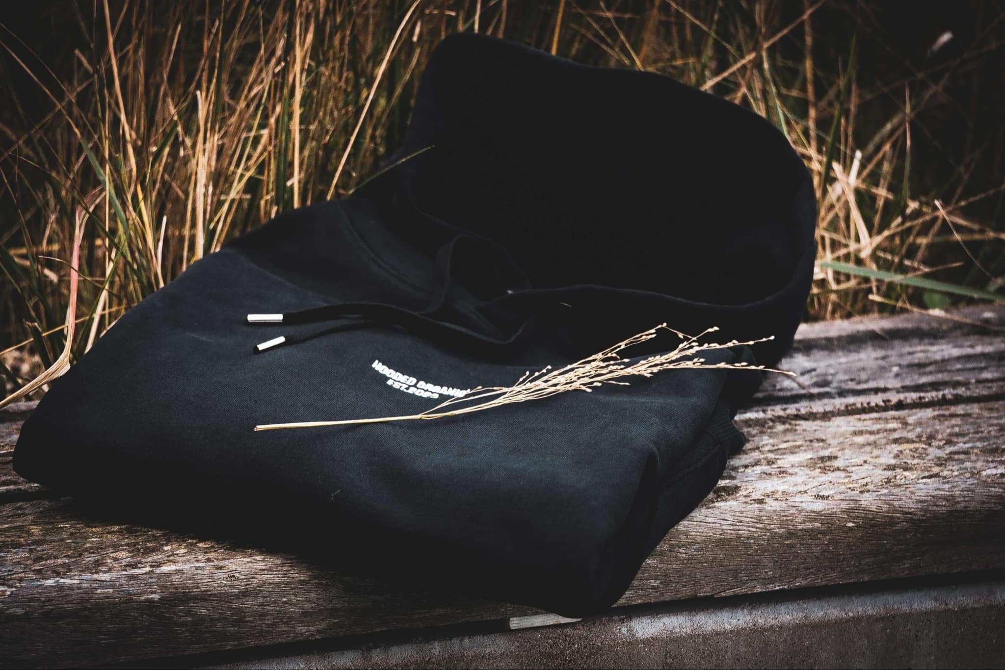Økologisk sort hoodie foldet på bænk i naturen – GOTS-certificeret og dansk design, lavet i Portugal